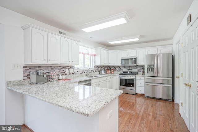 kitchen with decorative backsplash, a peninsula, stainless steel appliances, white cabinetry, and a sink