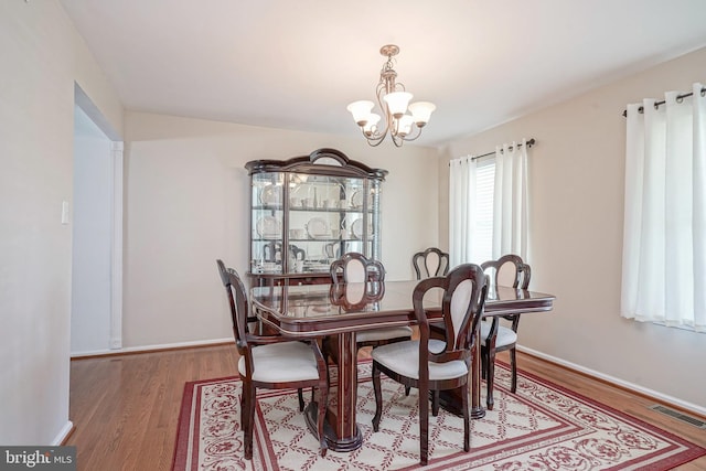 dining room with an inviting chandelier, baseboards, visible vents, and wood finished floors