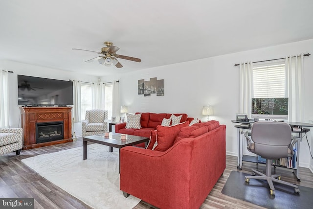 living room with ceiling fan, a glass covered fireplace, wood finished floors, and baseboards