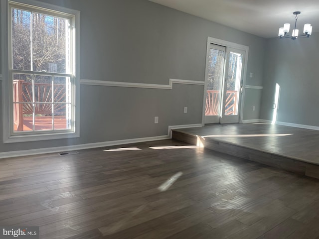 unfurnished dining area featuring dark wood finished floors, a notable chandelier, and baseboards