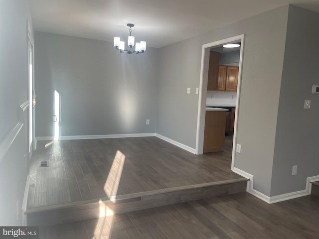 spare room featuring dark wood-style floors, baseboards, and a chandelier