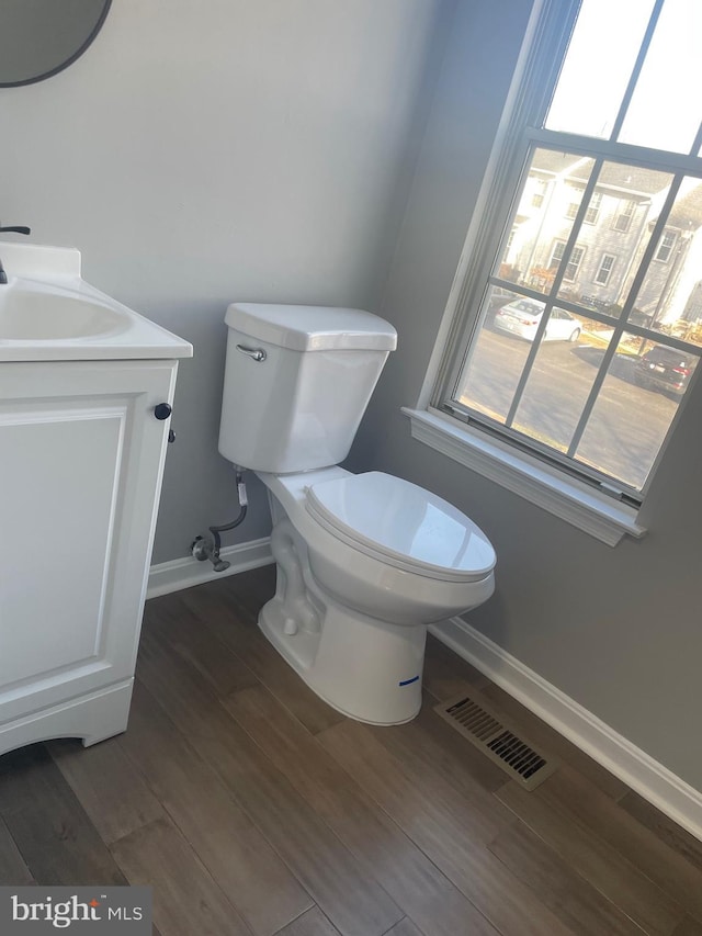 half bathroom featuring visible vents, baseboards, toilet, wood finished floors, and vanity