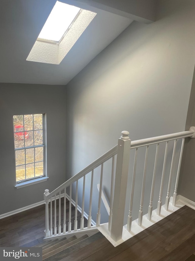 stairway with baseboards, wood finished floors, and a skylight