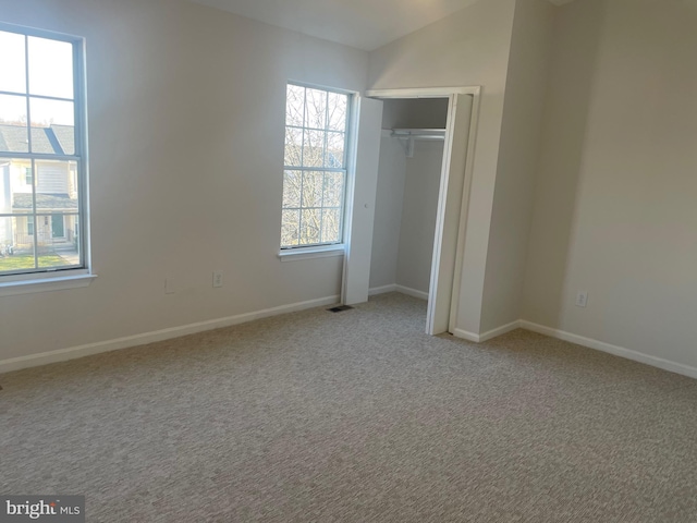 unfurnished bedroom featuring carpet, visible vents, baseboards, lofted ceiling, and a closet