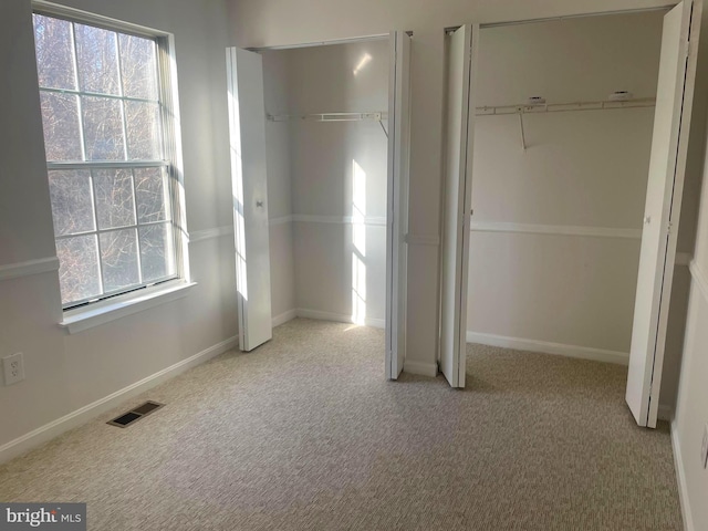 unfurnished bedroom with light carpet, visible vents, two closets, and baseboards