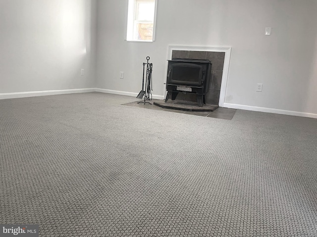 unfurnished living room featuring a wood stove, baseboards, and dark carpet