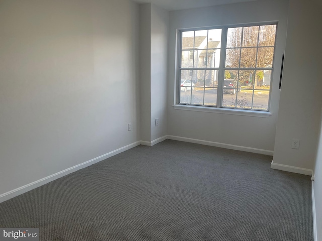 spare room featuring baseboards and dark carpet