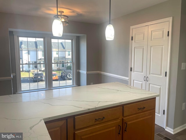 kitchen featuring light stone counters, decorative light fixtures, brown cabinets, and visible vents