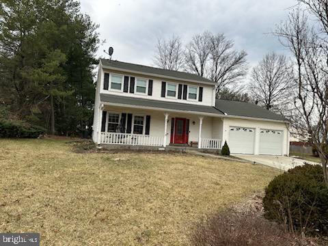 traditional-style home featuring an attached garage, covered porch, a front lawn, and concrete driveway