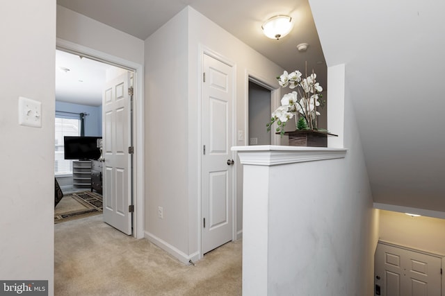 hallway with baseboards and light colored carpet