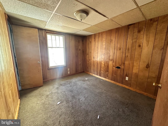 carpeted spare room featuring a drop ceiling, wooden walls, and baseboards