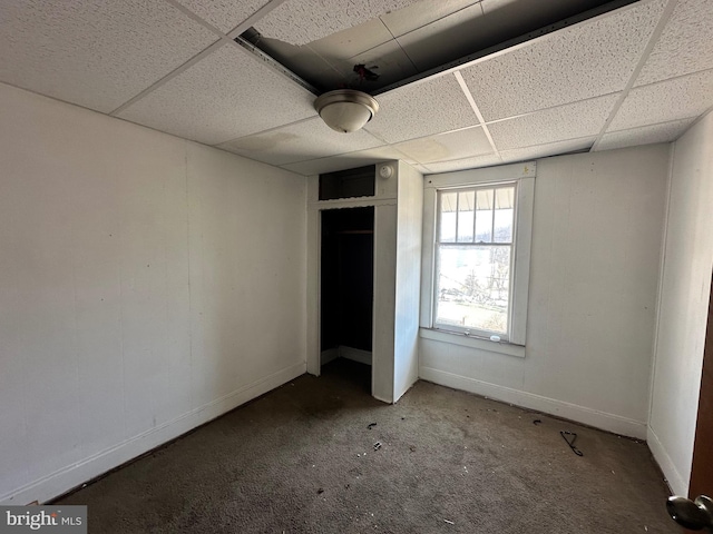 unfurnished bedroom with carpet, a closet, a drop ceiling, and baseboards