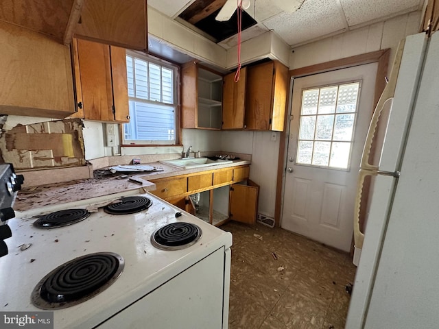 kitchen featuring a paneled ceiling, white appliances, a sink, light countertops, and brown cabinetry