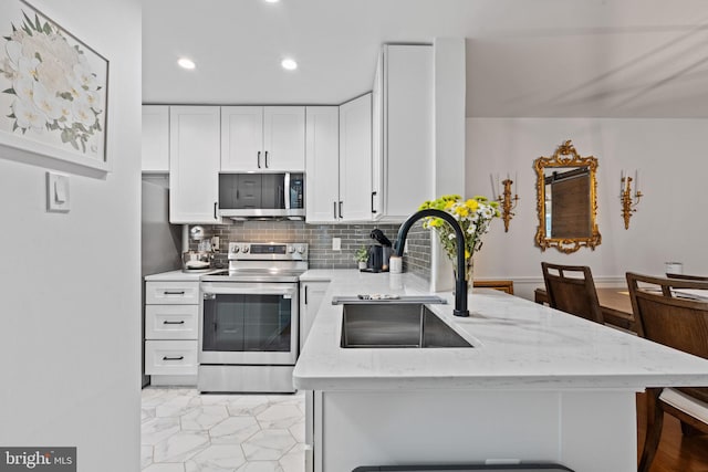 kitchen with stainless steel appliances, a peninsula, a sink, white cabinetry, and light stone countertops