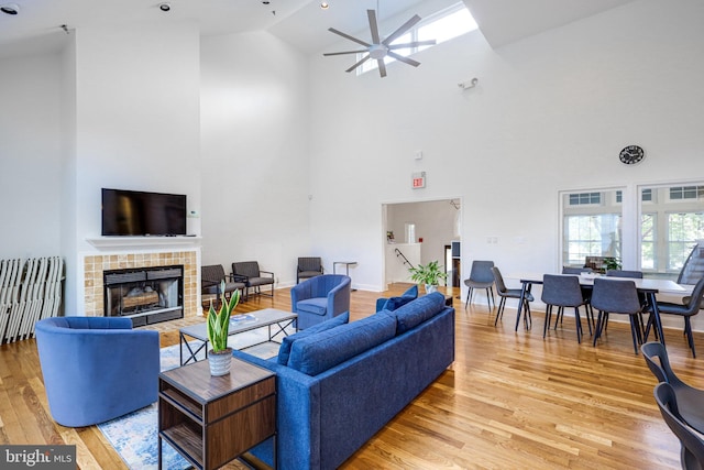 living room featuring ceiling fan, high vaulted ceiling, light wood-style flooring, a fireplace, and baseboards