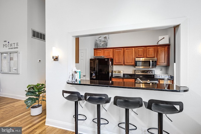 kitchen with appliances with stainless steel finishes, light wood-type flooring, visible vents, and a breakfast bar area