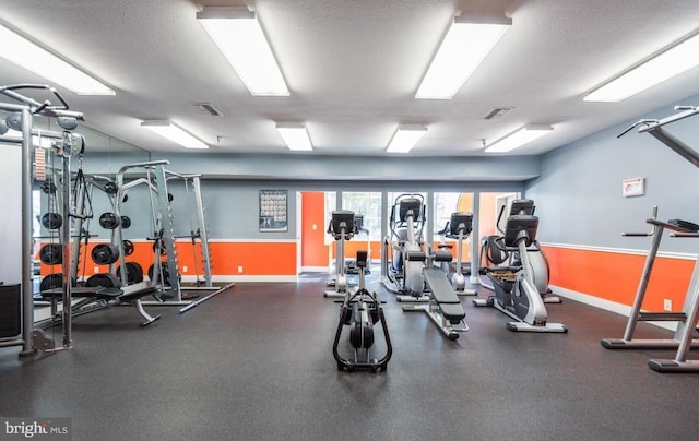 exercise room featuring a textured ceiling, visible vents, and baseboards