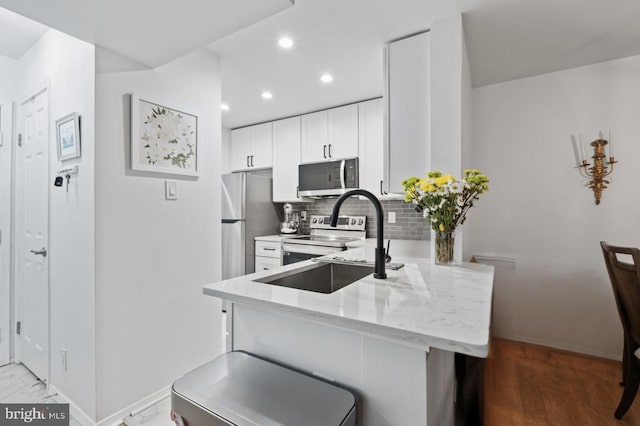 kitchen featuring tasteful backsplash, appliances with stainless steel finishes, a peninsula, light stone countertops, and white cabinetry