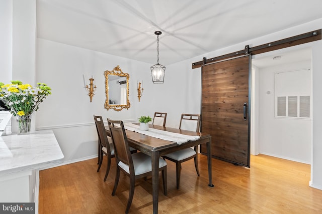 dining room with light wood-style floors, visible vents, baseboards, and a barn door