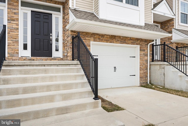 view of exterior entry featuring a garage, driveway, and a shingled roof