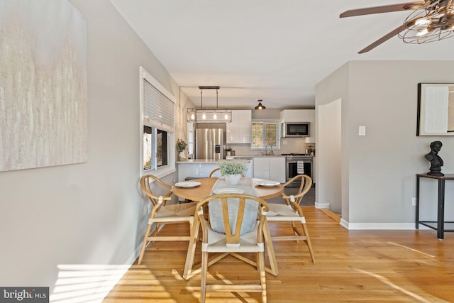 dining space featuring a ceiling fan, light wood-type flooring, and baseboards