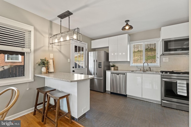 kitchen featuring backsplash, a breakfast bar, appliances with stainless steel finishes, white cabinetry, and a sink