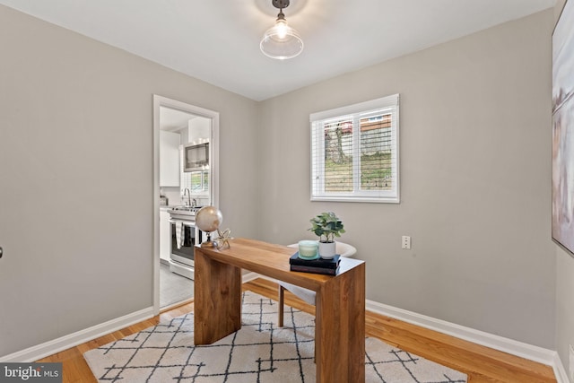 home office featuring a sink, baseboards, and light wood finished floors