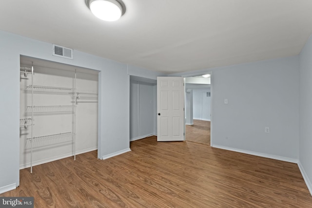 unfurnished bedroom featuring wood finished floors, visible vents, a closet, and baseboards