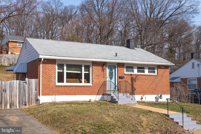 view of front of property with brick siding, a chimney, a front yard, and fence