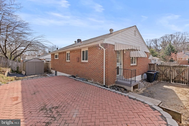 back of house with brick siding, a shed, an outbuilding, and fence