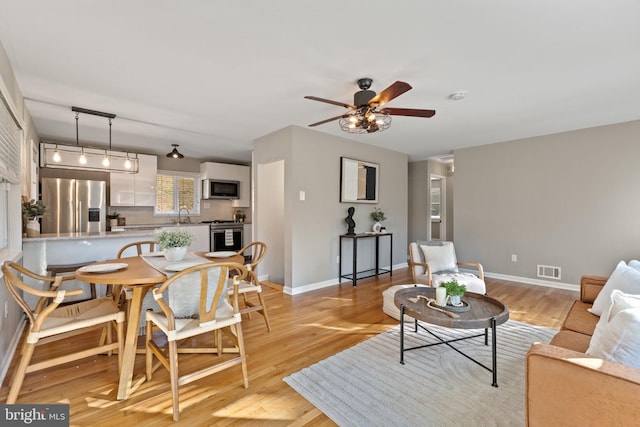 living area featuring a ceiling fan, visible vents, light wood finished floors, and baseboards