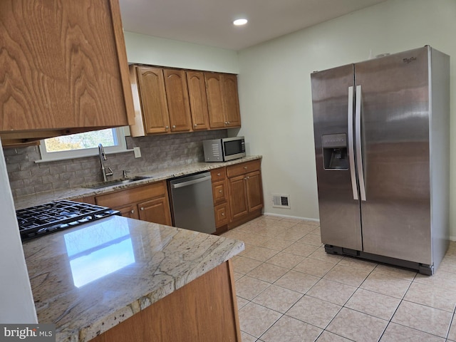 kitchen featuring light tile patterned floors, stainless steel appliances, visible vents, brown cabinetry, and a sink