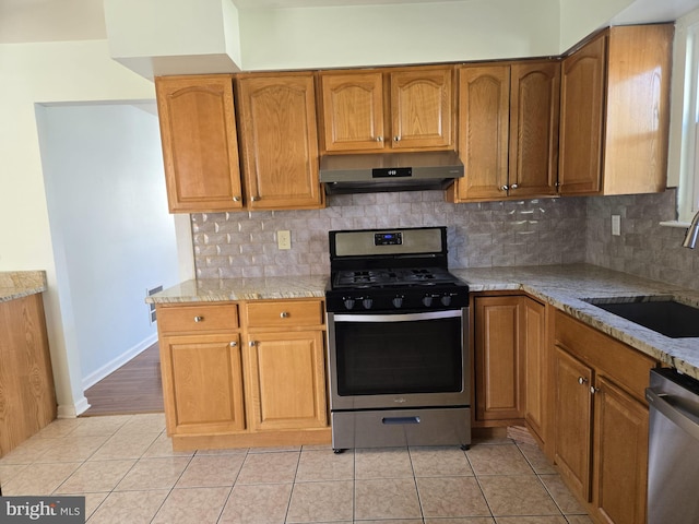 kitchen featuring light tile patterned floors, under cabinet range hood, a sink, appliances with stainless steel finishes, and light stone countertops