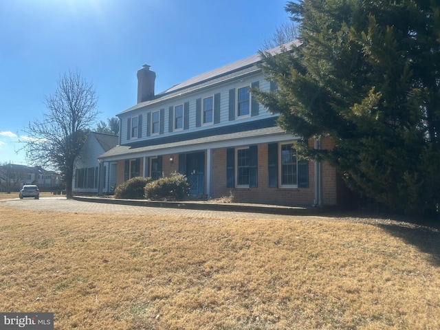 view of front of property with brick siding, a chimney, and a front yard