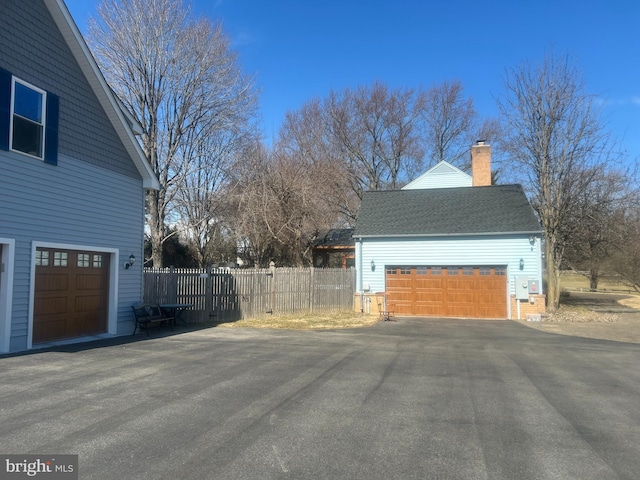 view of side of property featuring a garage, a shingled roof, a chimney, and fence