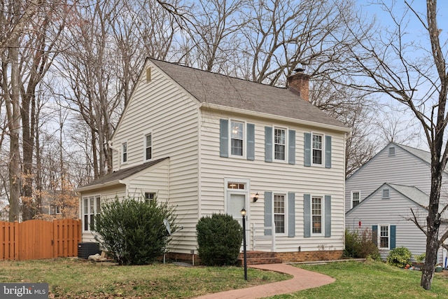 colonial-style house with central air condition unit, a chimney, fence, and a front lawn