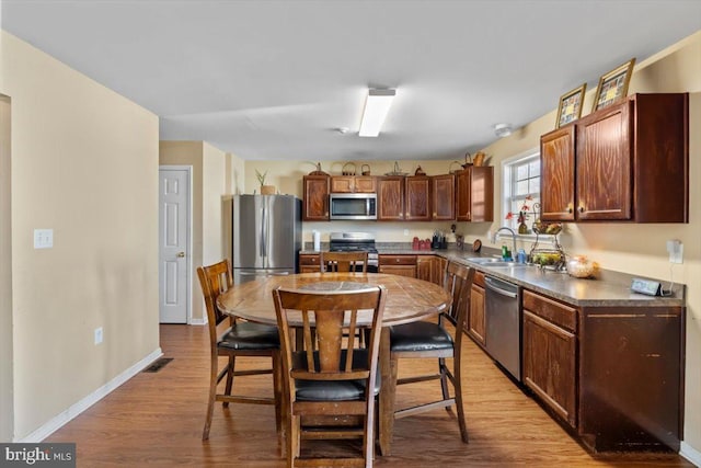 kitchen featuring stainless steel appliances, a sink, visible vents, baseboards, and light wood-style floors