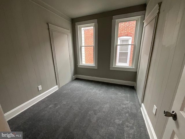 unfurnished bedroom with baseboards, wooden walls, and dark carpet