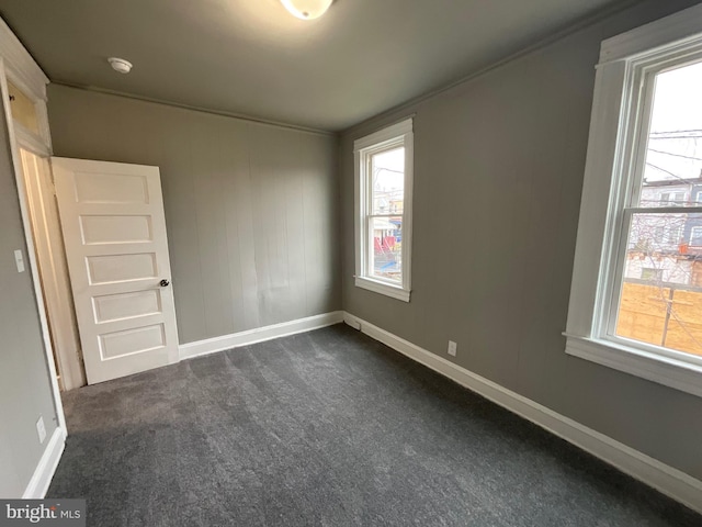 empty room featuring a wealth of natural light, baseboards, and dark carpet