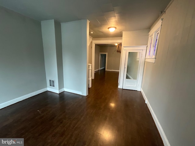 empty room with visible vents, dark wood-type flooring, and baseboards