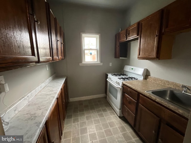 kitchen featuring a sink, light countertops, baseboards, dark brown cabinets, and white gas range