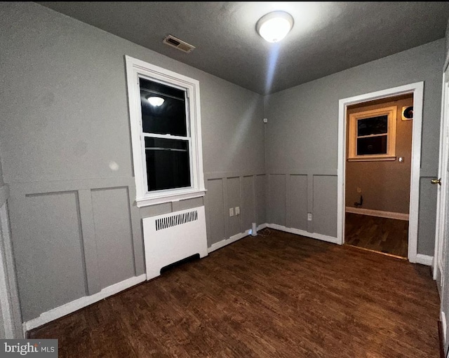 unfurnished room featuring dark wood-type flooring, radiator heating unit, visible vents, and a decorative wall