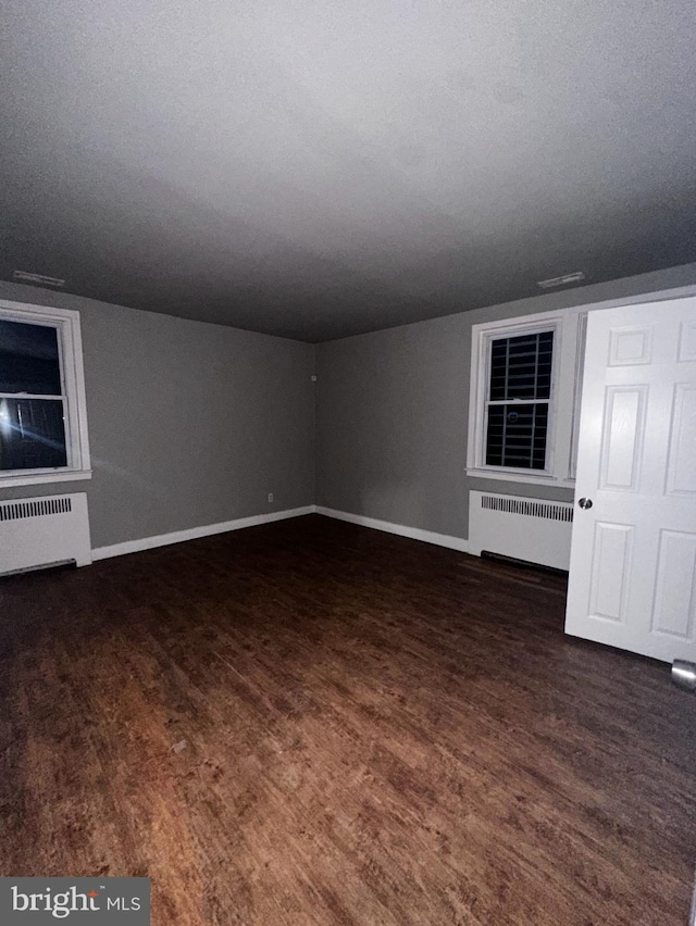 empty room featuring radiator heating unit, wood finished floors, and baseboards