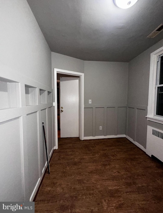 interior space with a decorative wall, a wainscoted wall, wood finished floors, visible vents, and radiator heating unit