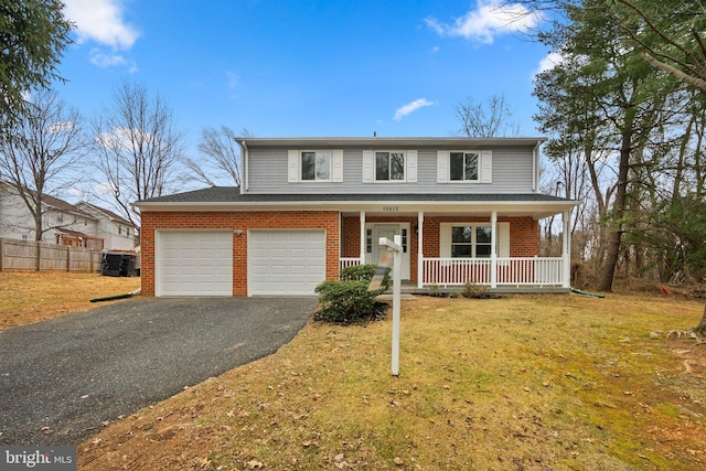 traditional-style home featuring a garage, aphalt driveway, covered porch, a front lawn, and brick siding