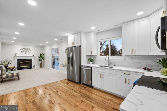 kitchen featuring white cabinets, decorative backsplash, appliances with stainless steel finishes, open floor plan, and a sink