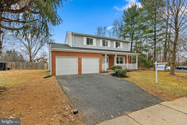 traditional home with aphalt driveway, brick siding, covered porch, fence, and a front lawn