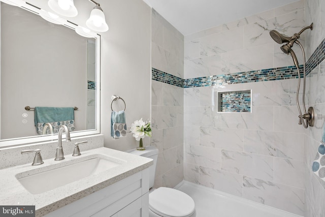 bathroom with toilet, tiled shower, and vanity