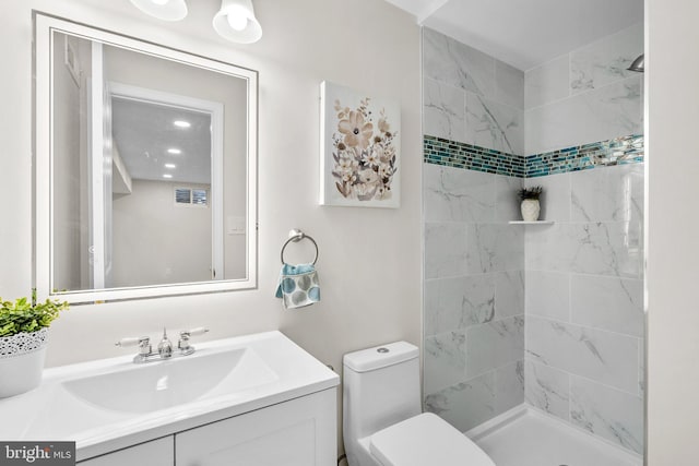 full bathroom with visible vents, tiled shower, vanity, and toilet