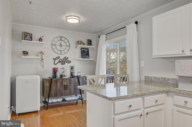 kitchen with a textured ceiling, light stone counters, light wood-style flooring, a peninsula, and white cabinets